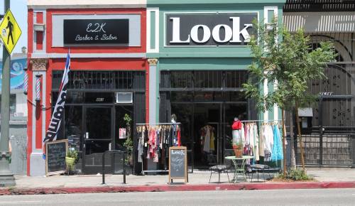 A colorful storefront featuring a salon and a clothing shop, with clothes displayed outside and a small seating area.