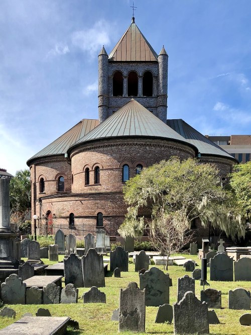 Historic round brick building with a tower, surrounded by a cemetery featuring weathered gravestones and lush greenery.