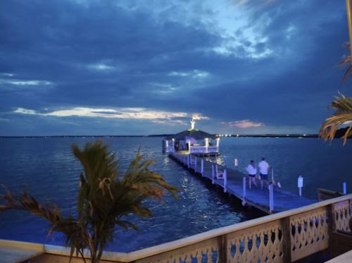 A serene twilight scene of a dock extending into calm waters, with two people sitting and a cloudy sky above.