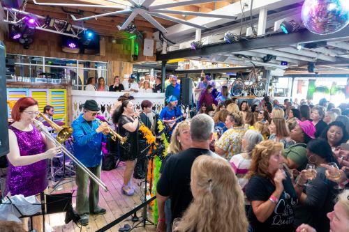A lively band performs on stage while a diverse crowd enjoys the music in a vibrant venue.