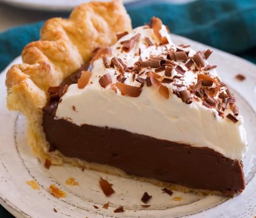 A slice of chocolate cream pie topped with whipped cream and chocolate shavings on a white plate.