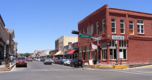 A sunny street scene featuring shops, cars, and a red brick building with "Isaacs" signage.