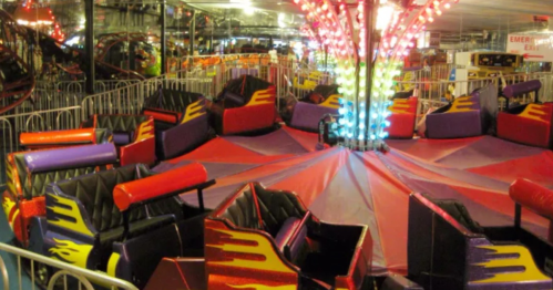 Colorful carnival ride with empty seats, surrounded by barriers and bright lights in a festive indoor setting.