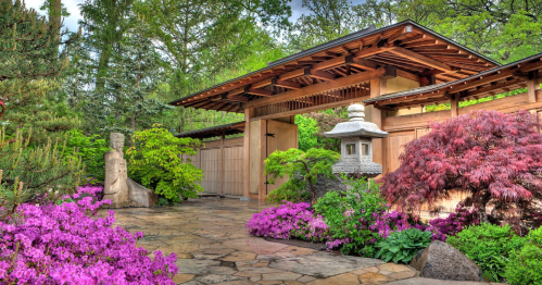 A serene garden entrance featuring lush greenery, vibrant flowers, and traditional stone lanterns.