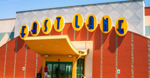 Entrance of a building with a colorful "FAST LANE" sign and a yellow awning. Clear blue sky in the background.