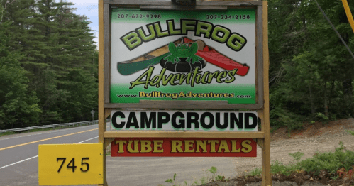 Sign for Bullfrog Adventures featuring campground and tube rentals, located along a tree-lined road.