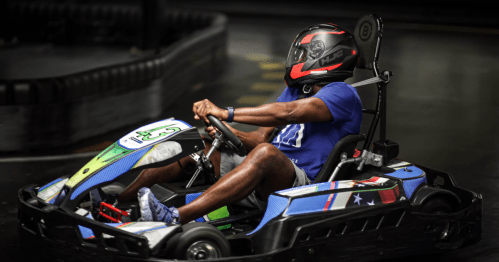 A person in a go-kart wearing a helmet, racing on a track with colorful designs on the kart.