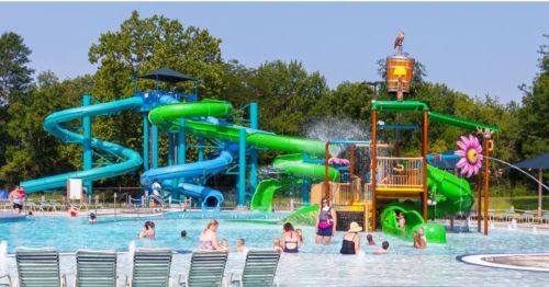 A vibrant water park with slides, a splash pad, and families enjoying the pool on a sunny day.