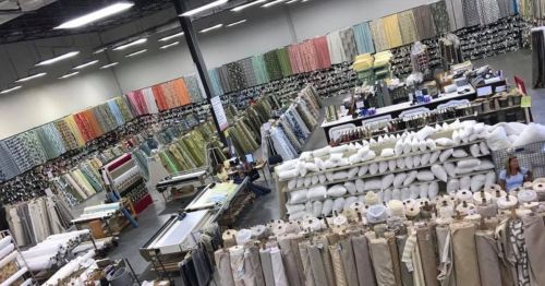 A spacious fabric store with colorful rolls of fabric and stacks of pillows arranged throughout the large interior.