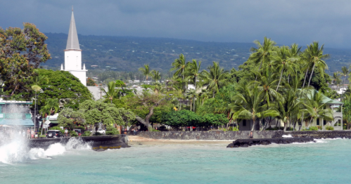 A coastal scene featuring palm trees, a church steeple, and waves crashing against a rocky shore under a cloudy sky.
