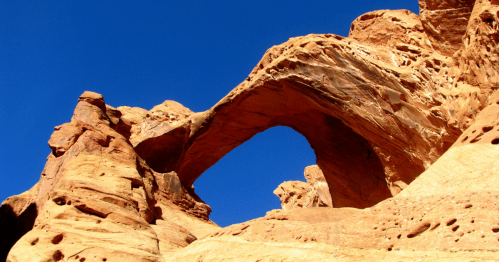 A natural rock arch stands tall against a clear blue sky, surrounded by rugged sandstone formations.