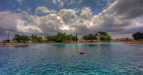 A serene swimming pool surrounded by trees and cloudy skies, with colorful floats scattered on the water's surface.