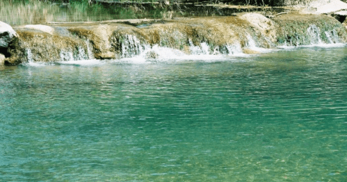 A serene water scene featuring a gentle waterfall cascading into a clear, turquoise pool.