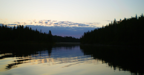 A serene lake at dusk, reflecting trees and a colorful sky with soft clouds.