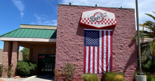 A pink building with a green roof, featuring a large American flag and a sign that reads "Peggy Sue's."