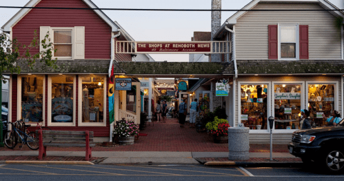 A charming street view of shops at Rehoboth Mews, featuring colorful storefronts and people walking in the evening light.