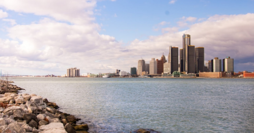 A view of a city skyline along a river, with modern buildings and a cloudy sky in the background.