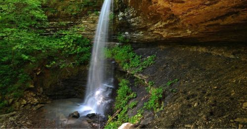 A serene waterfall cascades over rocky terrain, surrounded by lush green foliage and a tranquil pool below.
