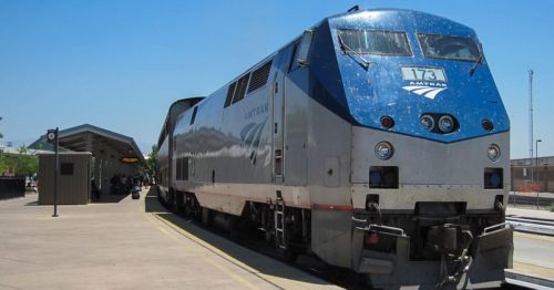 Amtrak train 173 at a station, with passengers waiting under a shelter on a sunny day.