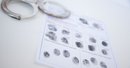 A fingerprint card displaying various fingerprints next to a pair of handcuffs.