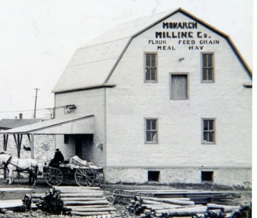 Historic black-and-white photo of the Monarch Milling Co. building with a horse-drawn cart in front.