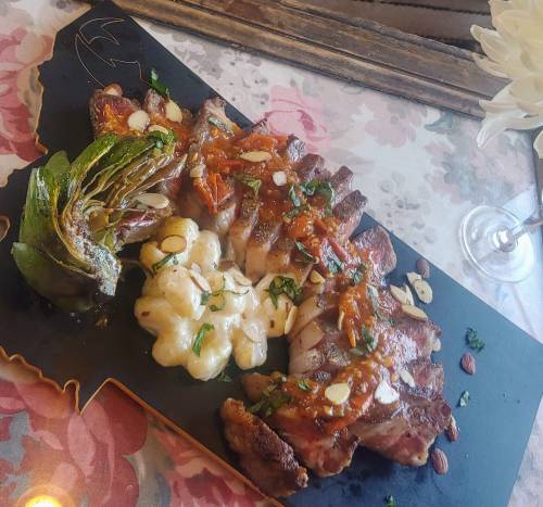 A gourmet dish featuring sliced meat, artichoke, creamy sauce, and garnishes on a decorative black platter.