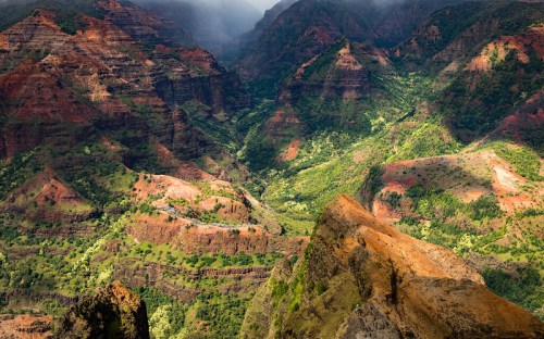 A breathtaking view of layered red and green mountains under a cloudy sky, showcasing dramatic natural landscapes.