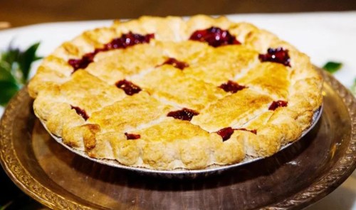 A golden-brown pie with a lattice crust and berry filling, displayed on a decorative plate.