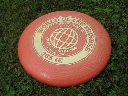 A red frisbee with "World Class Frisbee" and a globe design, resting on green grass.