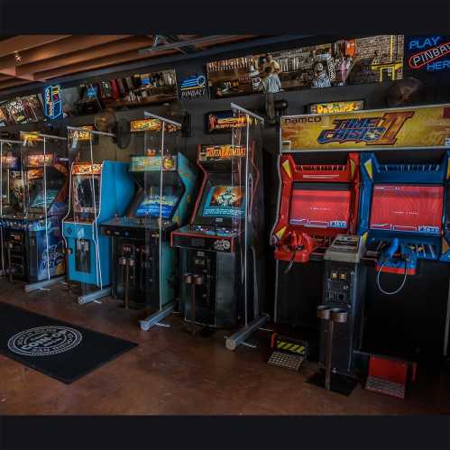 A vibrant arcade featuring classic video game machines and pinball tables in a retro setting.