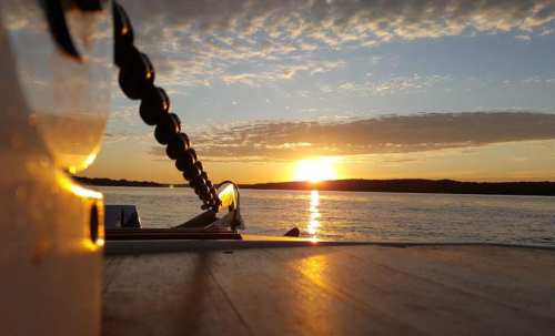 A serene sunset over water, viewed from a boat, with clouds reflecting warm colors in the sky.