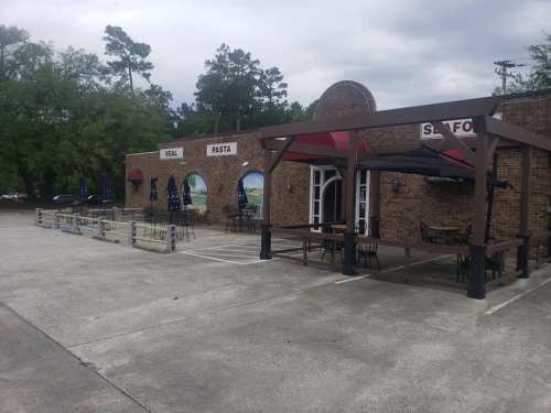 Exterior of a brick restaurant with outdoor seating, umbrellas, and signs for "Veal," "Pasta," and "Seafood."