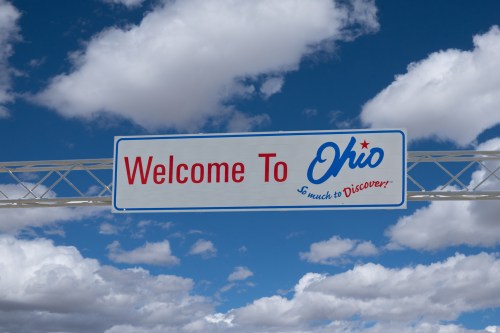 Sign welcoming visitors to Ohio, featuring blue skies and fluffy clouds in the background.