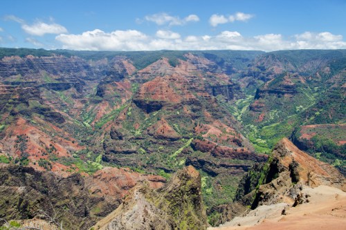 A panoramic view of a colorful canyon with steep cliffs and lush greenery under a bright blue sky.