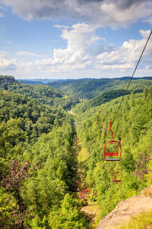 A scenic view of a chairlift over lush green hills and valleys under a partly cloudy sky.