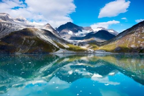 A serene mountain landscape reflecting in a clear blue lake, surrounded by snow-capped peaks and a bright sky.