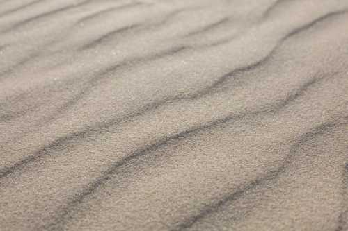 Close-up of textured sand with gentle waves and ripples, creating a natural pattern.