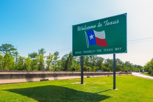 A green welcome sign for Texas featuring the state flag and the text "Drive Friendly - The Texas Way."
