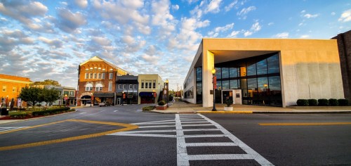 A street view of a small town with historic buildings and modern architecture under a cloudy blue sky.