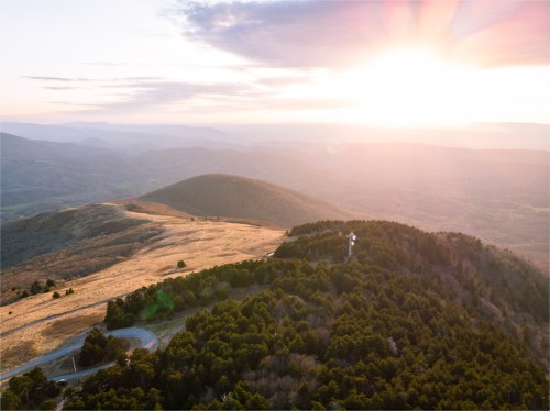 Aerial view of rolling hills at sunset, with a tower on a hill and a winding road below.