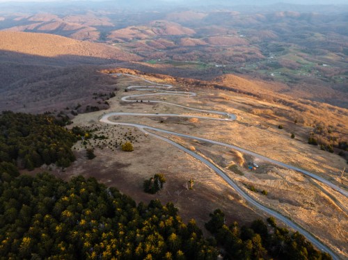 Aerial view of winding roads through hilly terrain, surrounded by trees and mountains under a golden sunset.