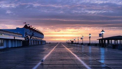 A serene boardwalk at sunrise, with colorful clouds and lights lining the path, creating a peaceful atmosphere.