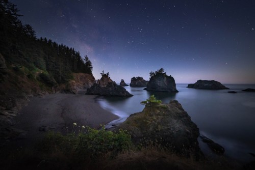 A serene coastal scene at night, featuring rocky formations and a starry sky above a calm ocean.