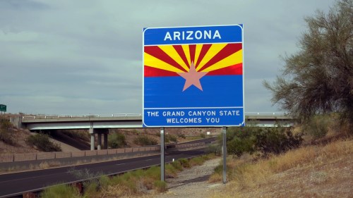 Welcome sign for Arizona featuring the state flag design and text: "The Grand Canyon State Welcomes You."