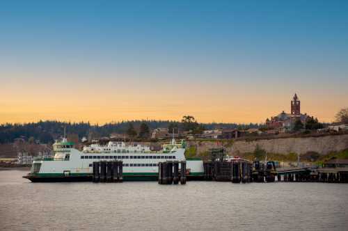 A ferry docked at a pier with a scenic sunset and a distant building on a hillside.