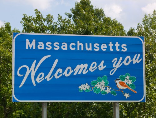 A blue welcome sign for Massachusetts featuring flowers and a bird, with the text "Massachusetts Welcomes You."