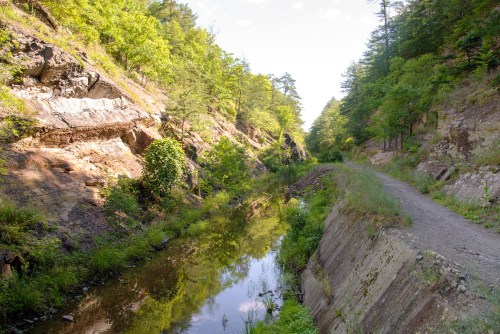A serene landscape featuring a narrow waterway flanked by rocky cliffs and lush greenery under a clear blue sky.