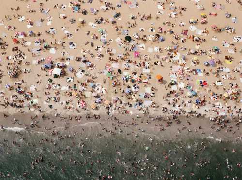 Aerial view of a crowded beach with colorful umbrellas, towels, and people enjoying the sun and water.