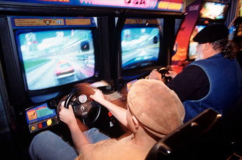 Two people playing racing arcade games, focused on the screens while steering their game controllers.