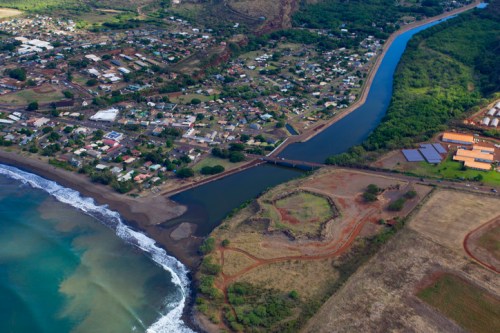 Aerial view of a coastal town with a river, lush greenery, and a beach, showcasing residential areas and natural landscapes.